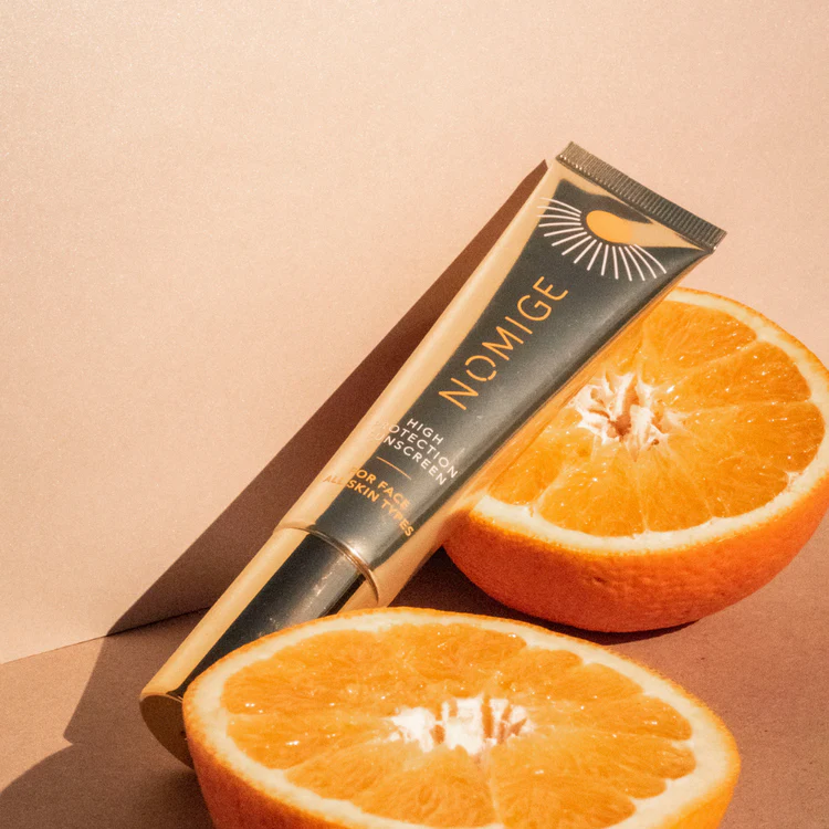 A sunscreen tube next to halved oranges on a beige background.