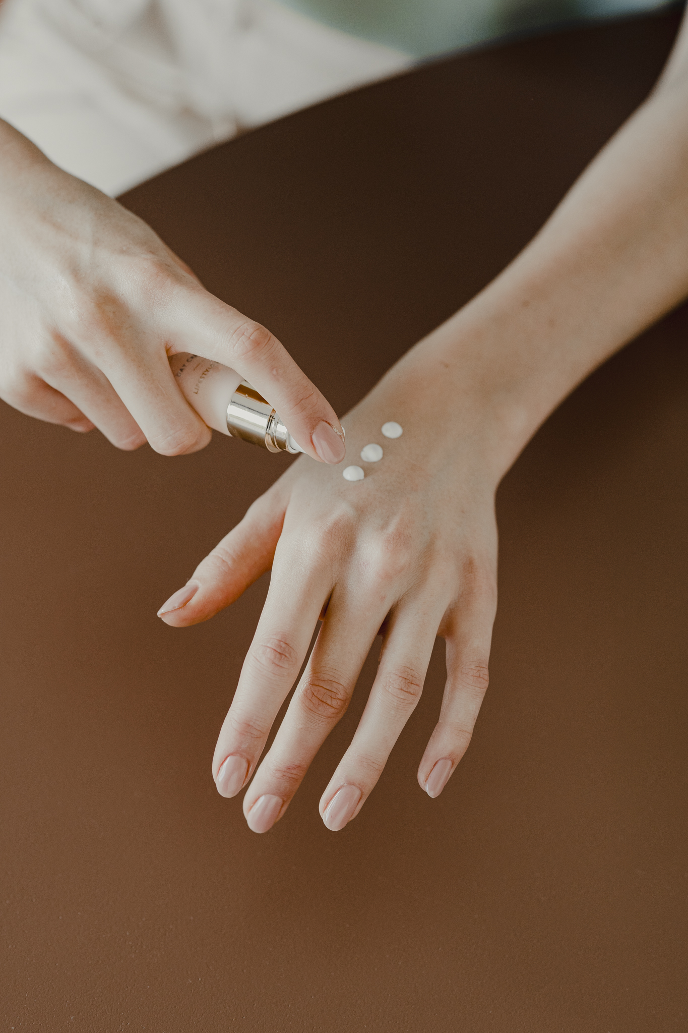 A person dispenses three drops of white lotion from a pump bottle onto the back of their hand.