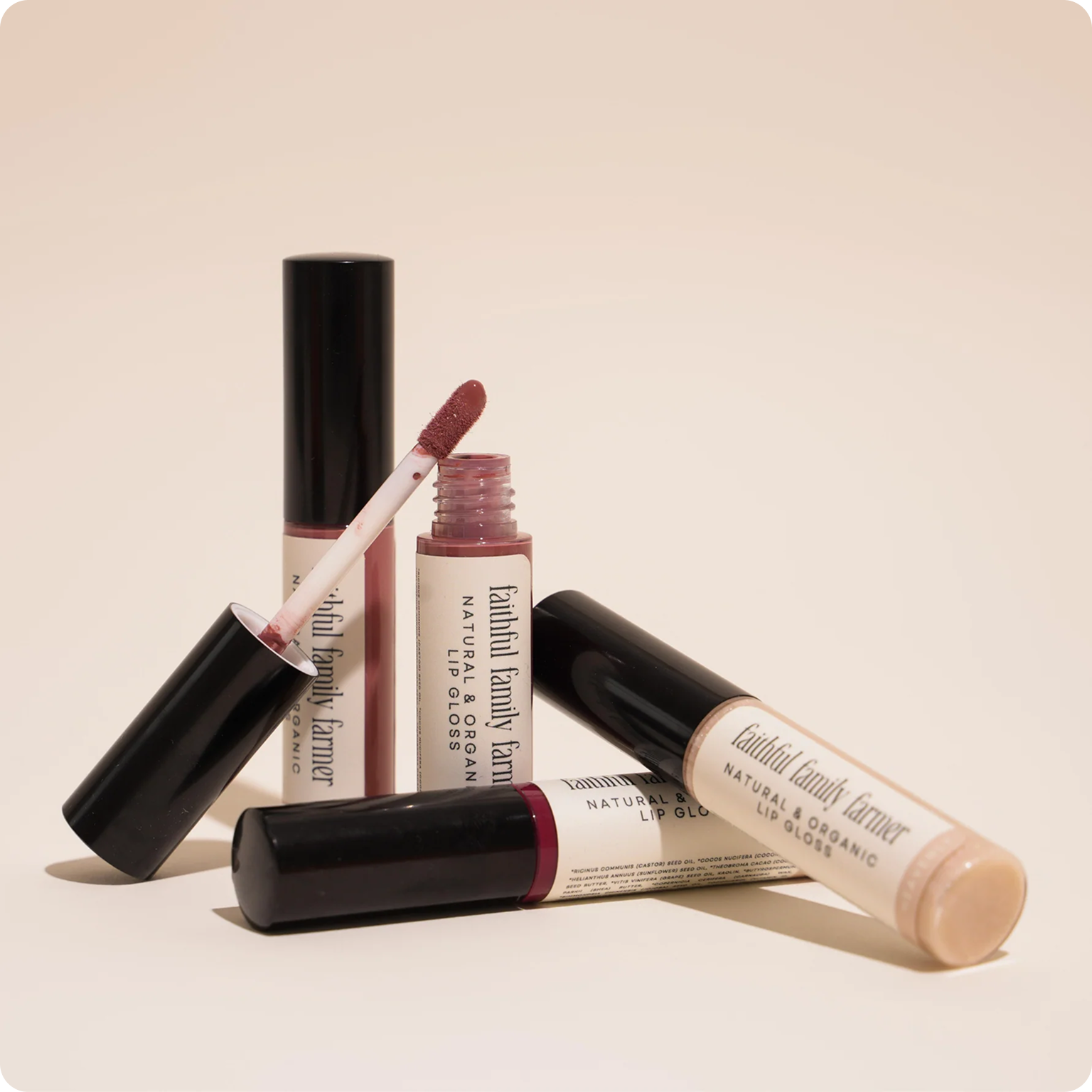 Several tubes of Faithful Family Farmer Natural & Organic Lip Gloss against a light, neutral background.