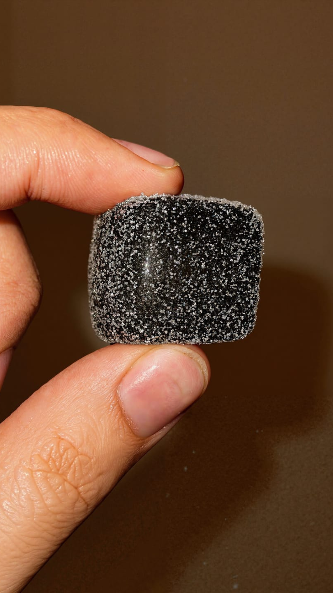 A hand holding a sugar-coated black candy.
