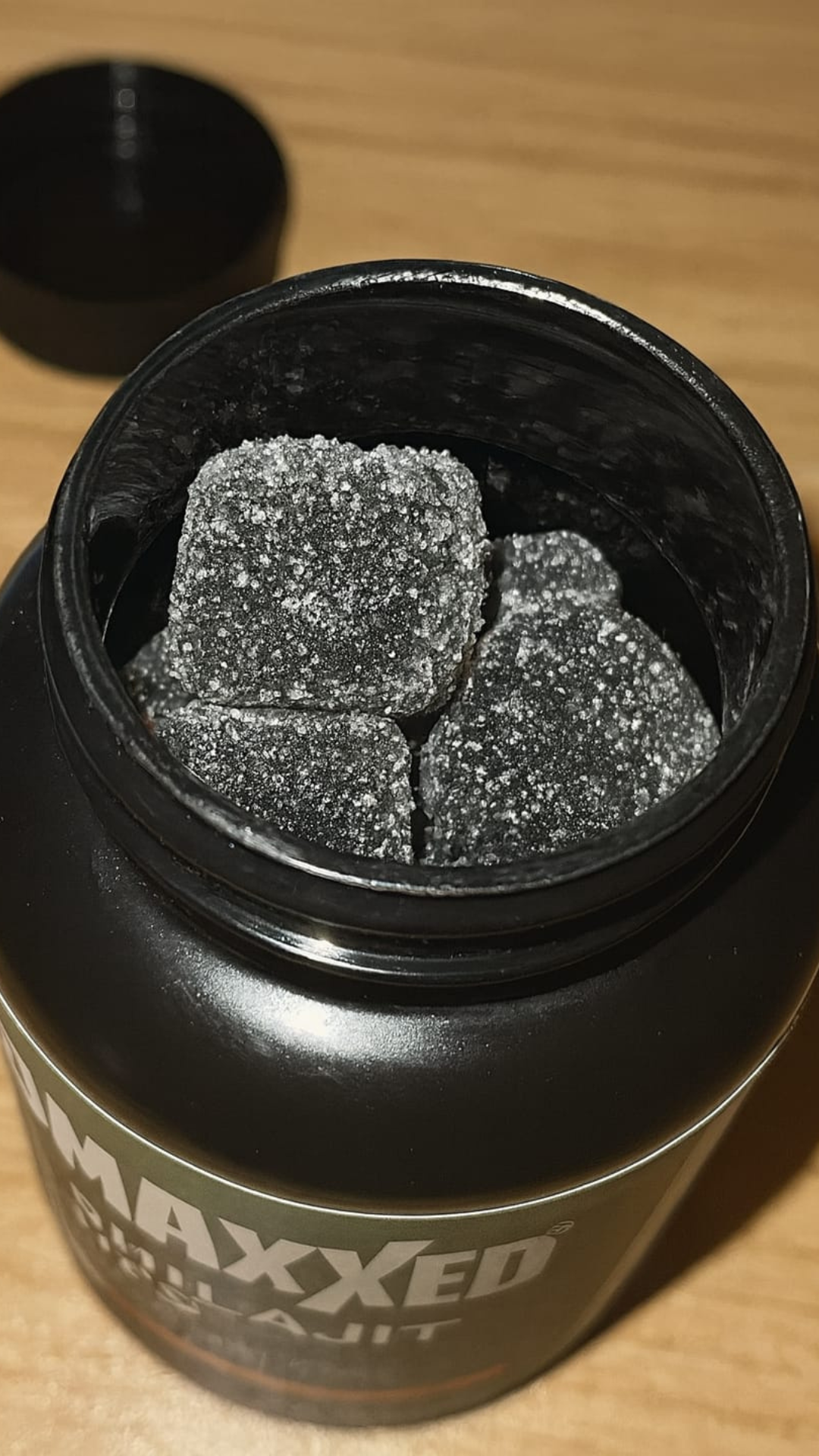 Black jar with sugar-coated square candies inside on a wooden surface.