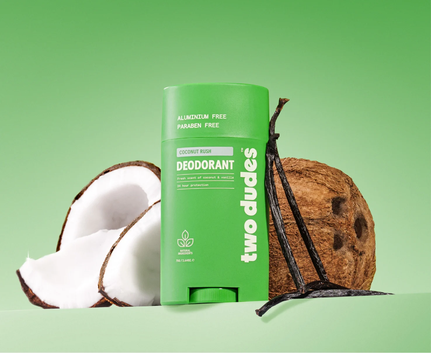 A green stick of Two Dudes deodorant is displayed next to a split coconut and vanilla beans.