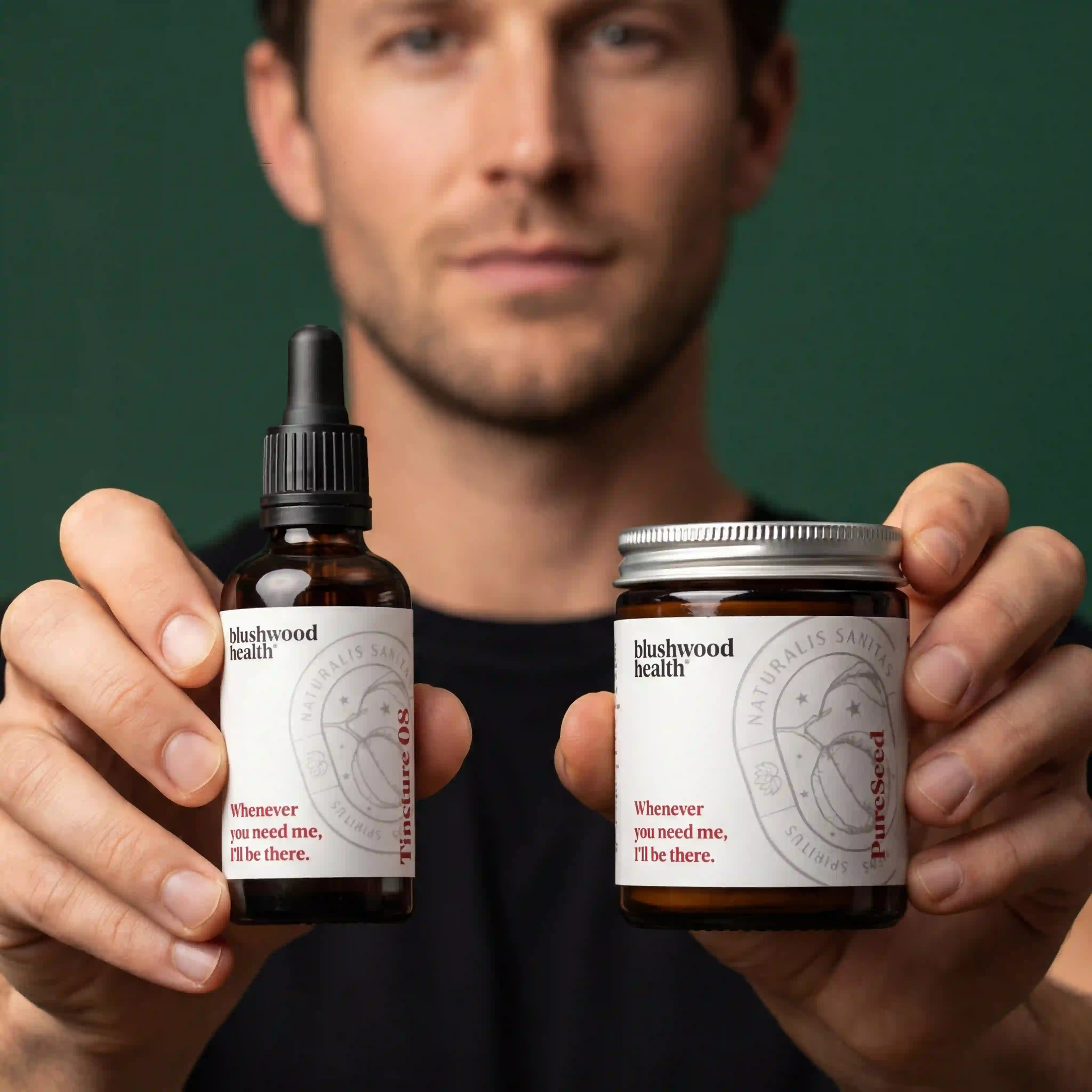 A man holds up a tincture bottle and a small jar from Blushwood Health against a green background.