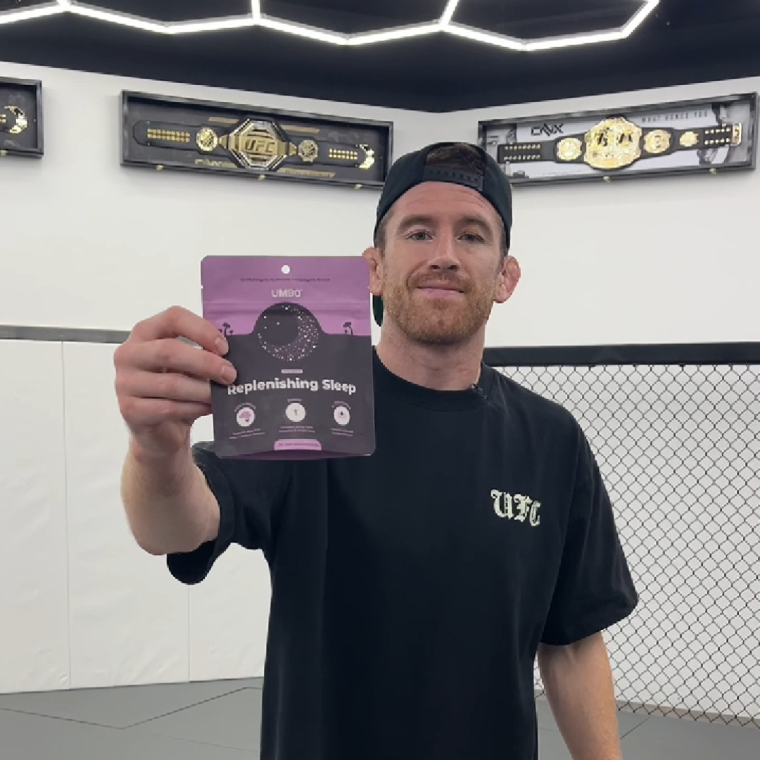 Person holding a sleep supplement package in a gym with championship belts on the wall.