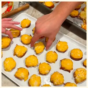 Two hands reaching for small, round, yellow appetizers on a white rectangular platter.