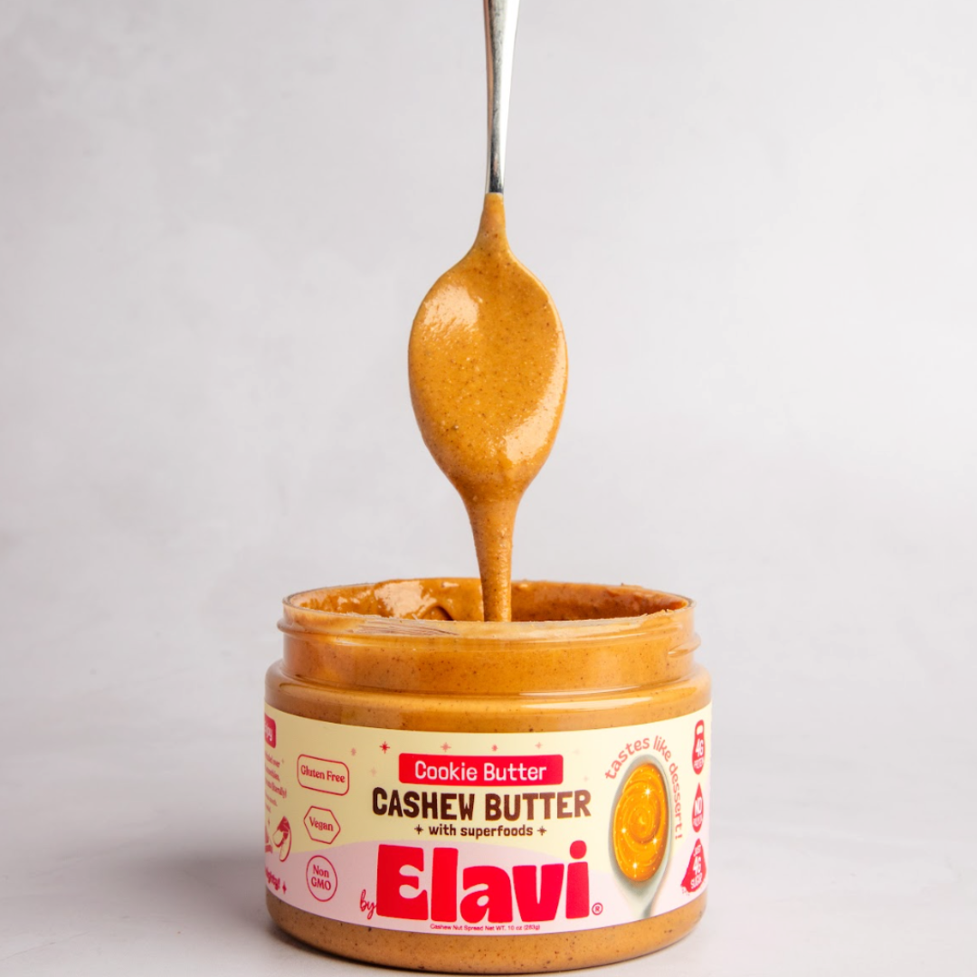 Spoon dripping cashew butter into an open jar labeled 'Elavi Cookie Butter Cashew Butter.'