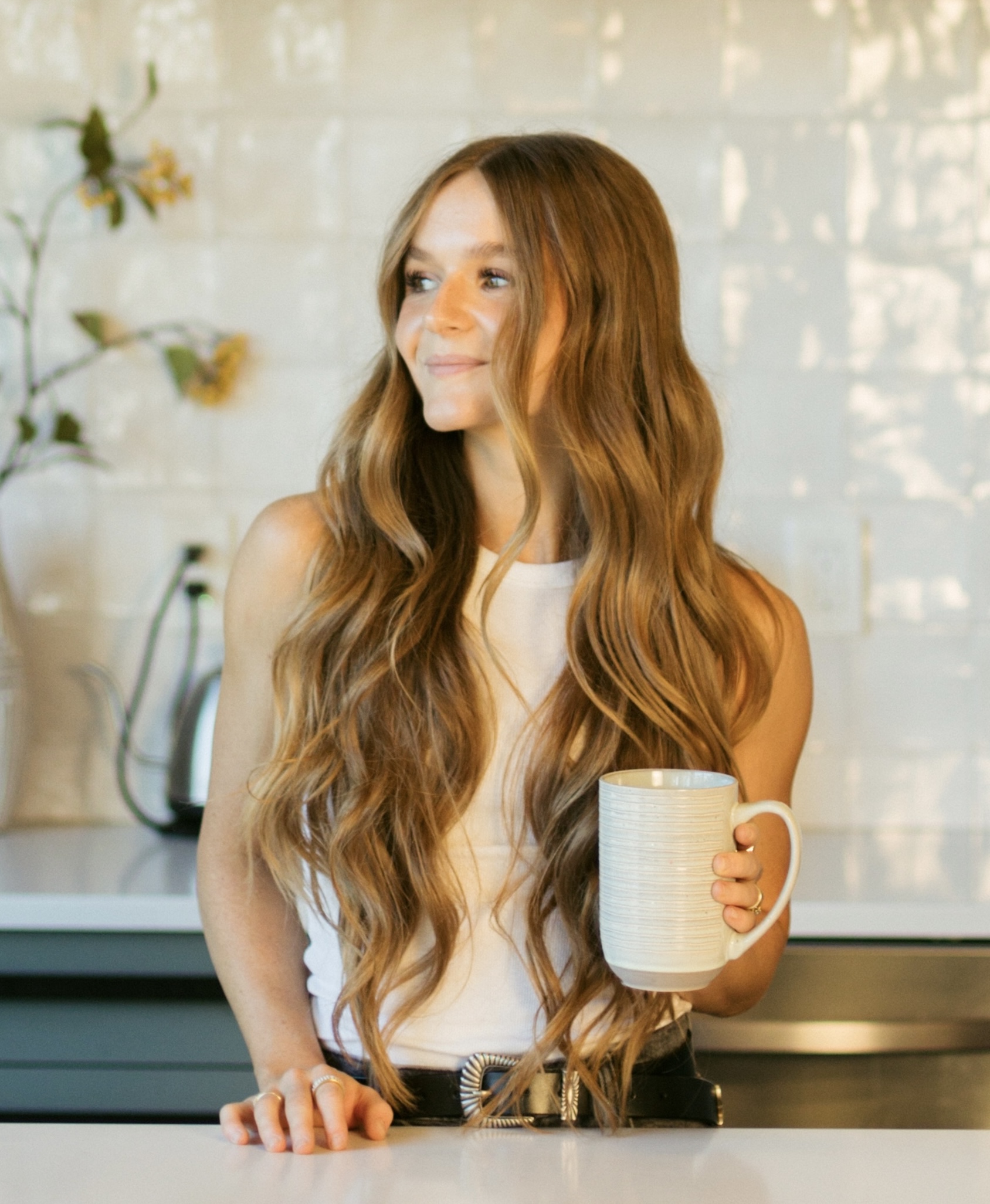 Woman with long hair holding a mug in a kitchen setting.