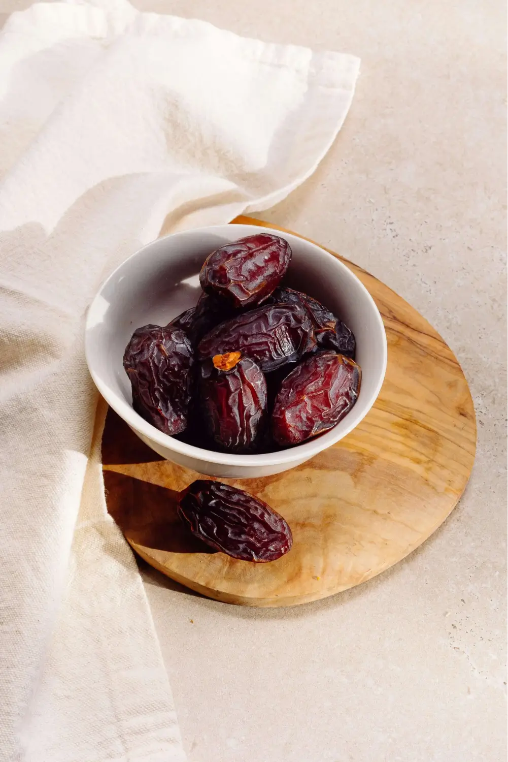 Bowl of dates on a wooden board with a cloth beside it.