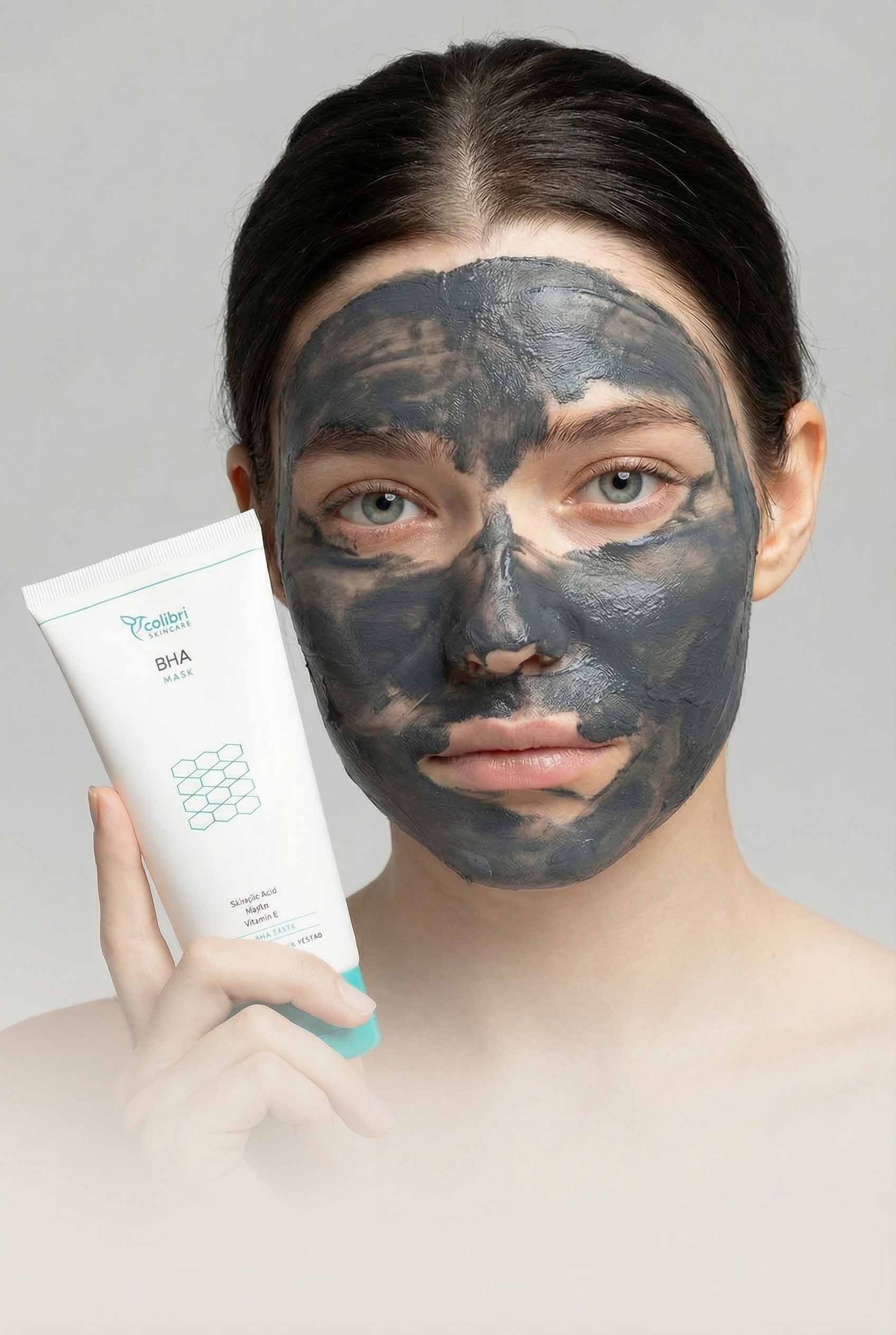 Person with a clay mask holding a BHA face mask tube.
