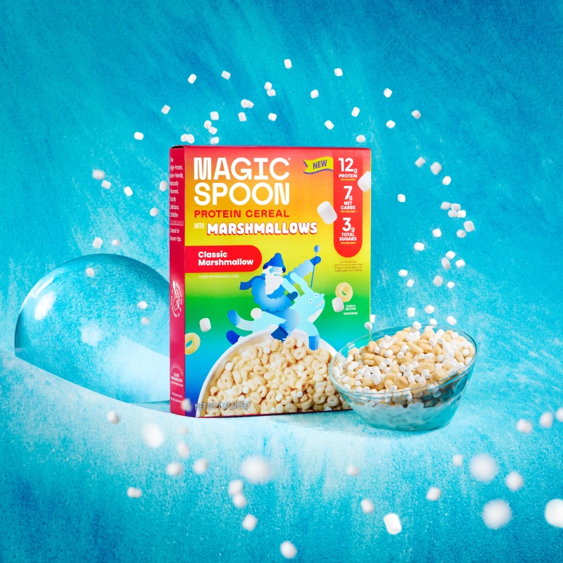 A box of Magic Spoon marshmallow protein cereal next to a glass bowl of the same cereal.
