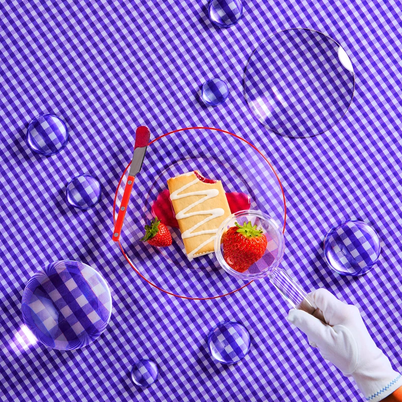 A gloved hand holds a magnifying glass over a strawberry and pastry on a purple gingham tablecloth.