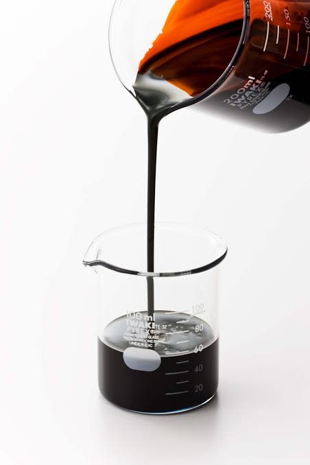 Dark liquid being poured into a clear lab beaker.
