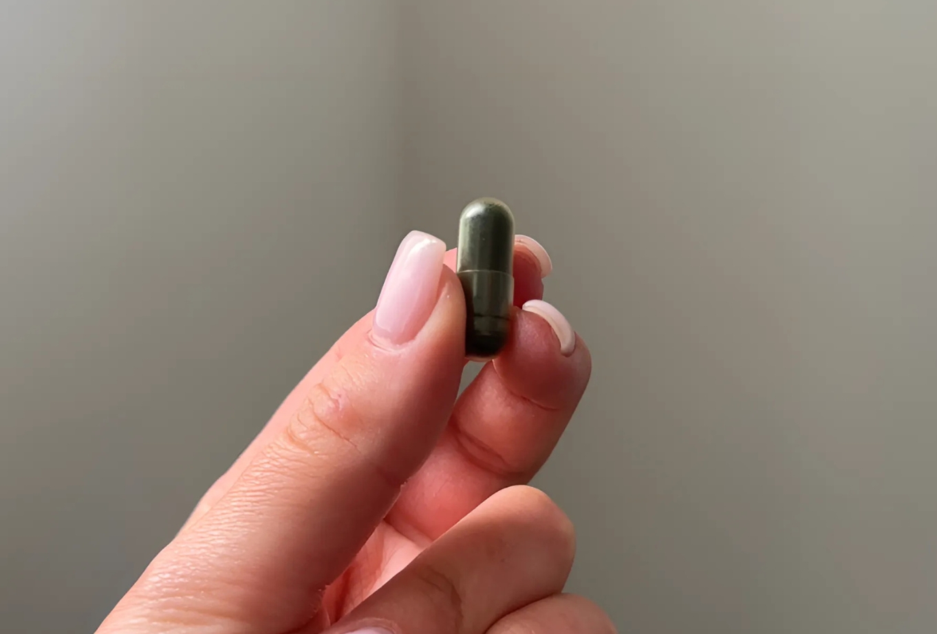 A hand holding a small green capsule against a plain background.