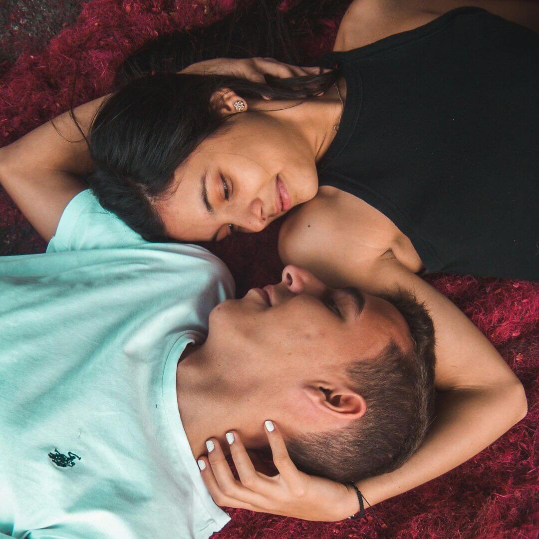 Two people lying on a red surface, looking at each other affectionately.