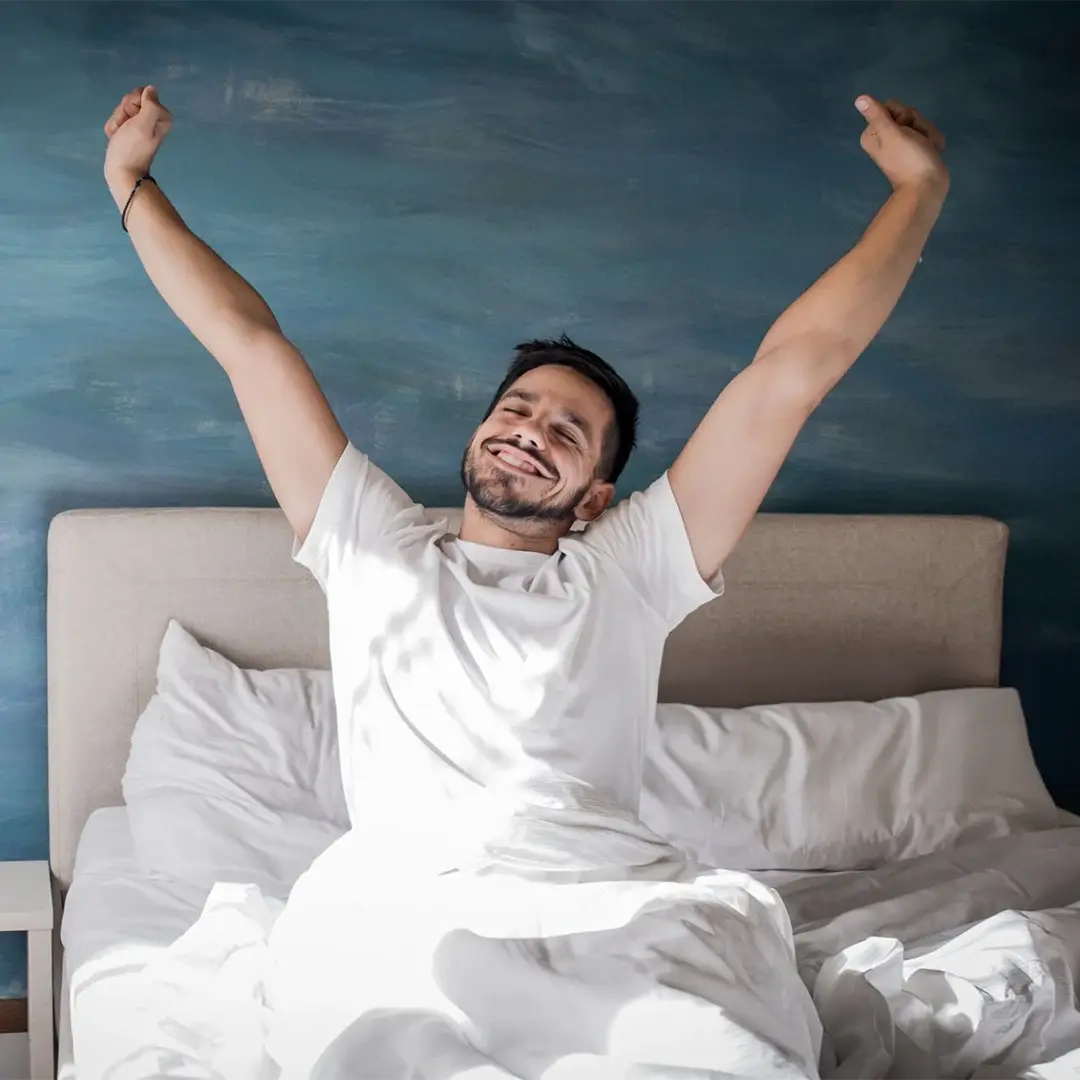 Person stretching happily in bed with blue wall background.