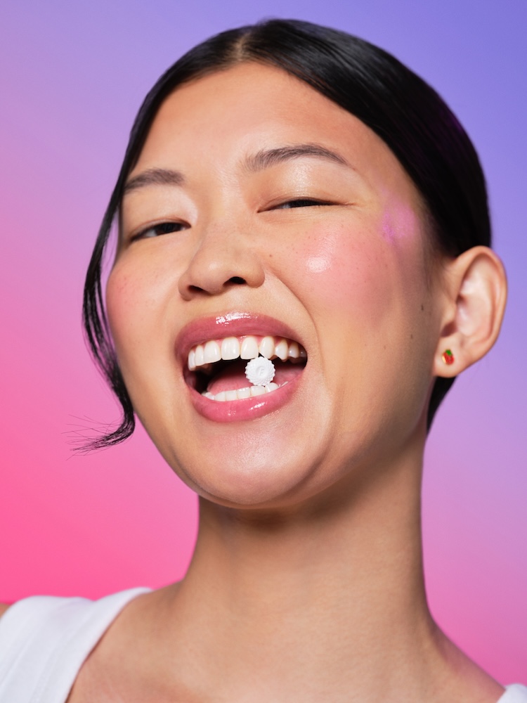 Person smiling with a small flower between teeth against a gradient background.