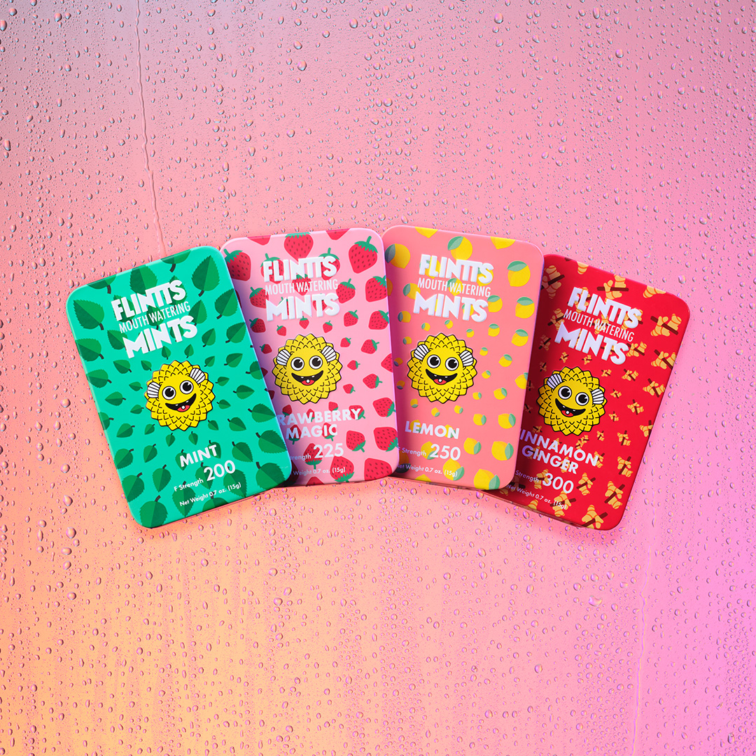Four colorful mint tins with a smiling sun design on a dewy pink background.