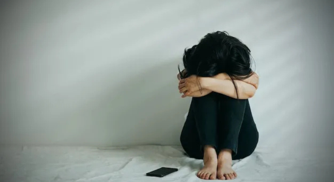 Person sitting on the floor with head down, phone nearby.