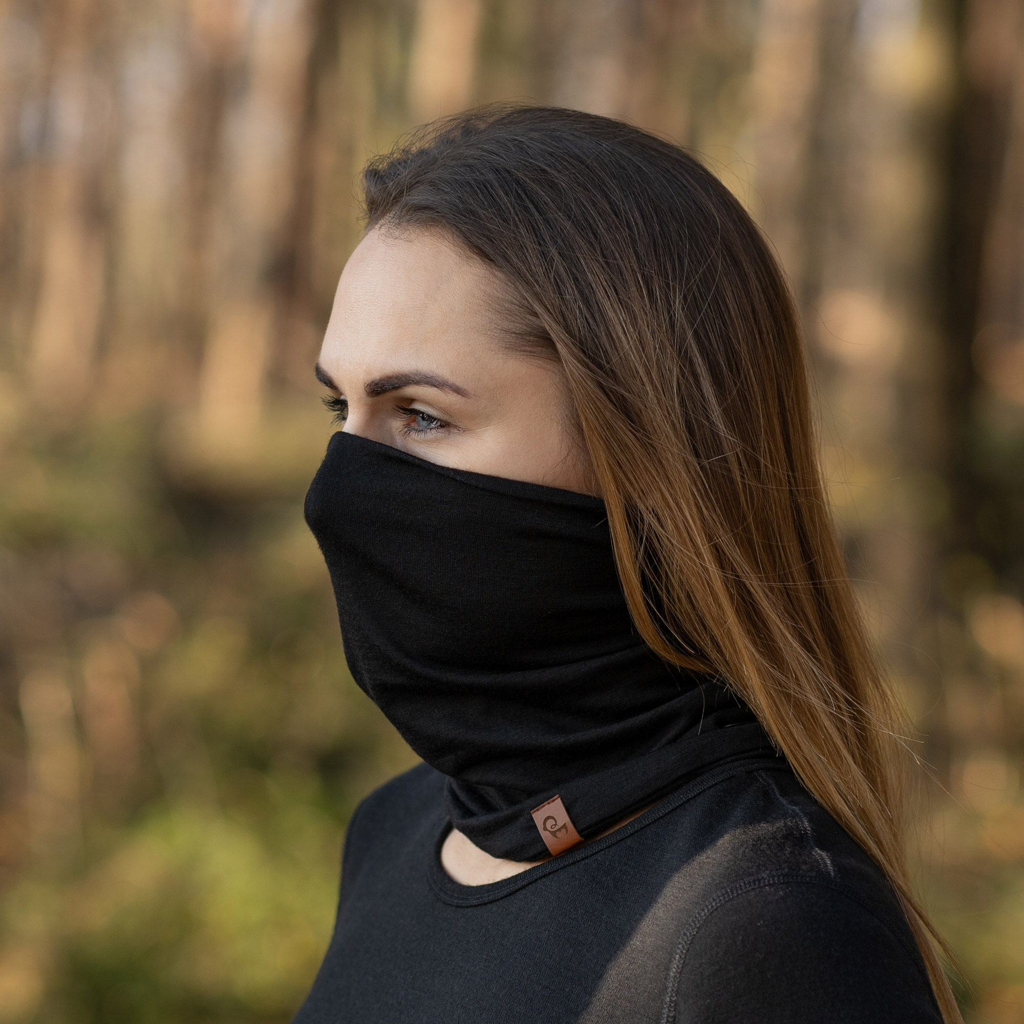 A woman with long brown hair looks to her left while wearing a black neck gaiter outdoors.
