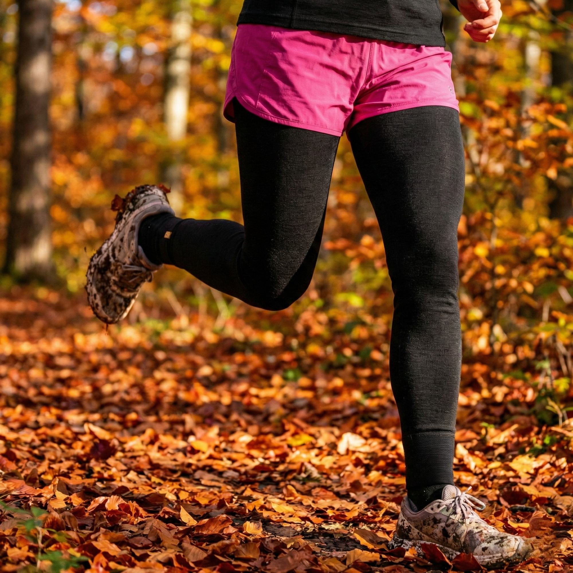Close-up of a person's legs running through fallen autumn leaves in a forest.