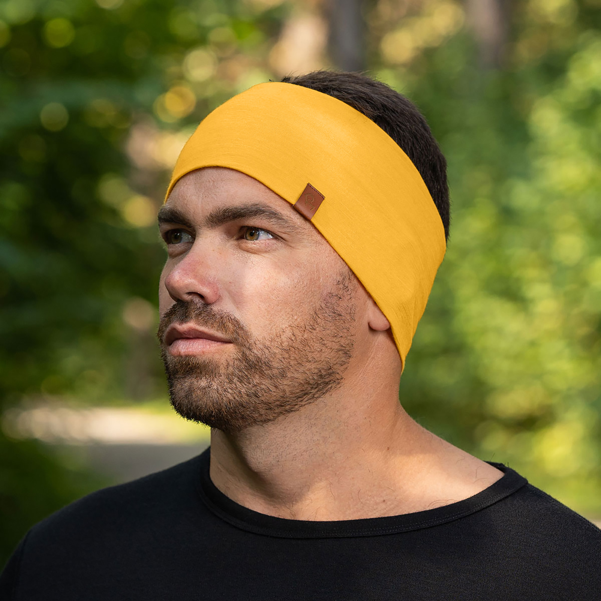 A man with a beard wearing a wide yellow headband and a black t-shirt outdoors.