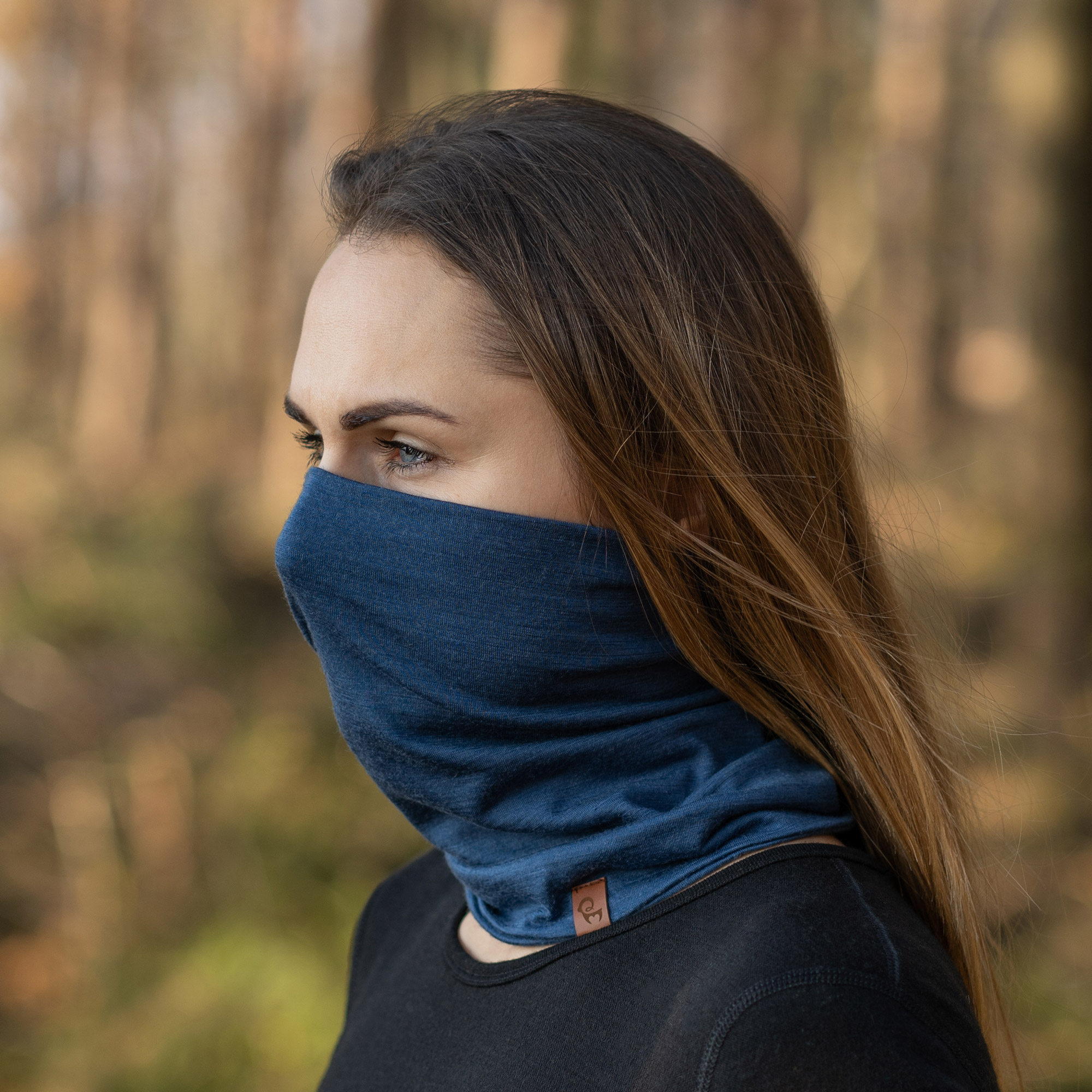 A woman with long brown hair wears a blue neck gaiter pulled up over her nose and mouth.