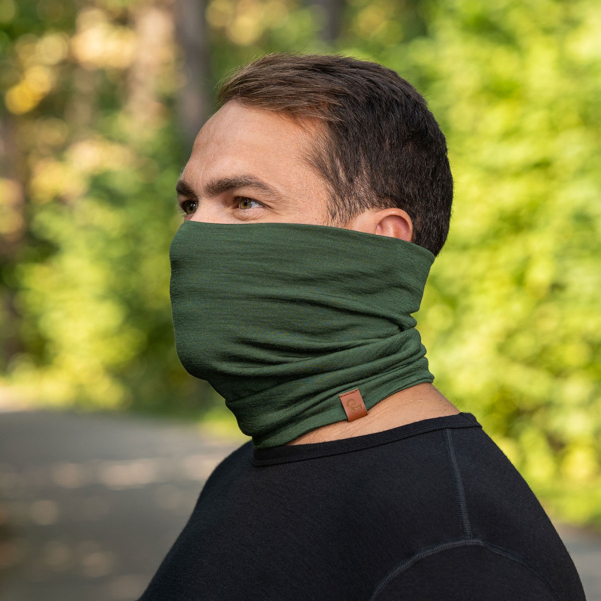 A man in profile wears a green neck gaiter pulled up over his nose and mouth outdoors.