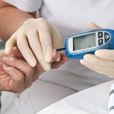 Gloved hands using a glucose meter on an elderly person's hand.