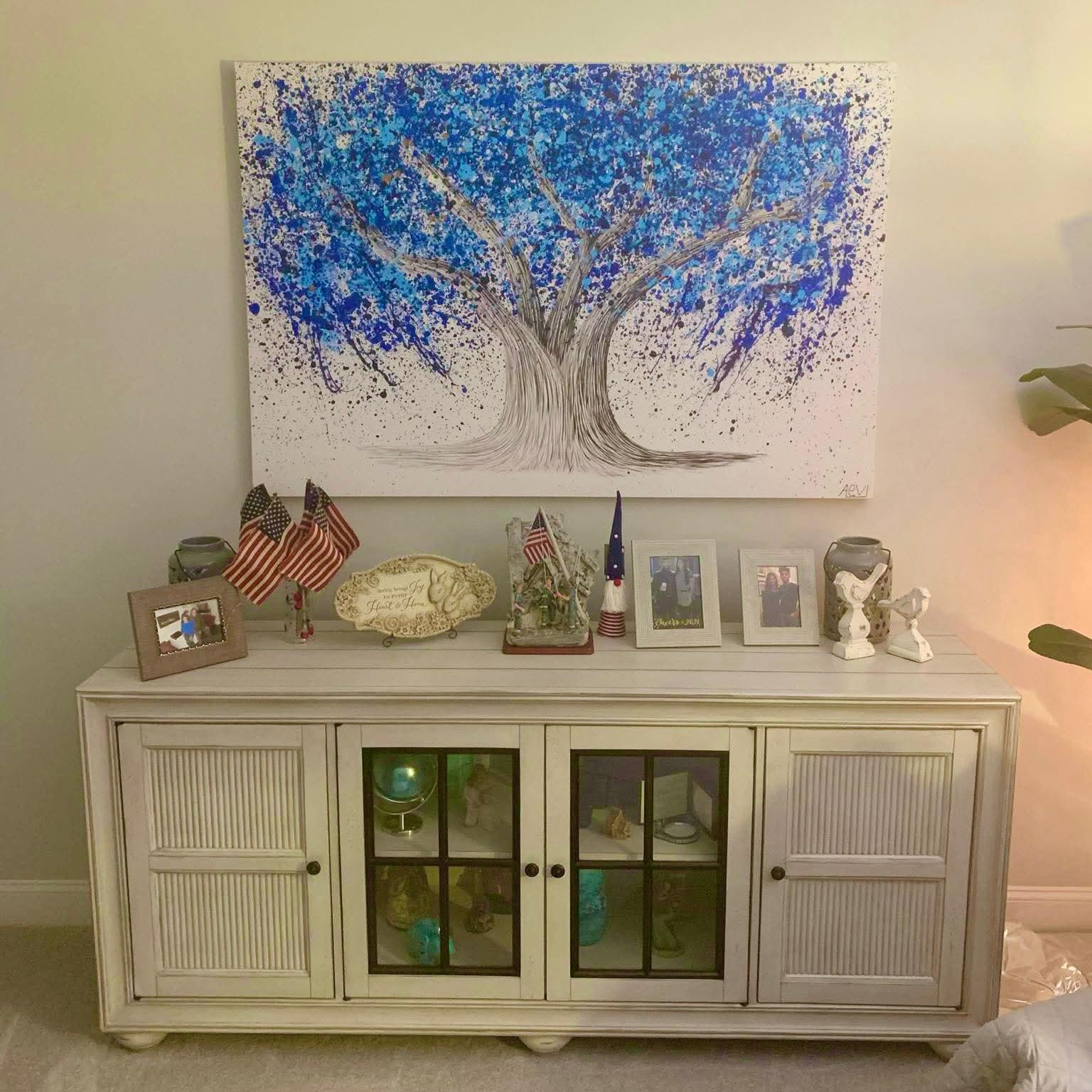 White cabinet with framed photos, American flags, and a blue tree painting above.