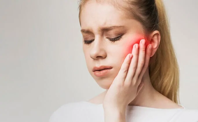 A young woman holds her jaw in pain, with a red glow indicating the source of her discomfort.