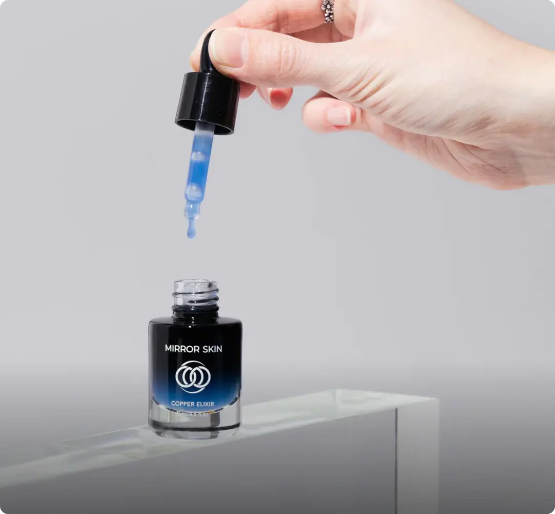 A hand holds a bottle of Mirror Skin serum over another bottle resting on a stone surface.