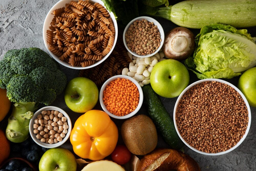 Assorted fruits, vegetables, grains, and legumes on a gray surface.