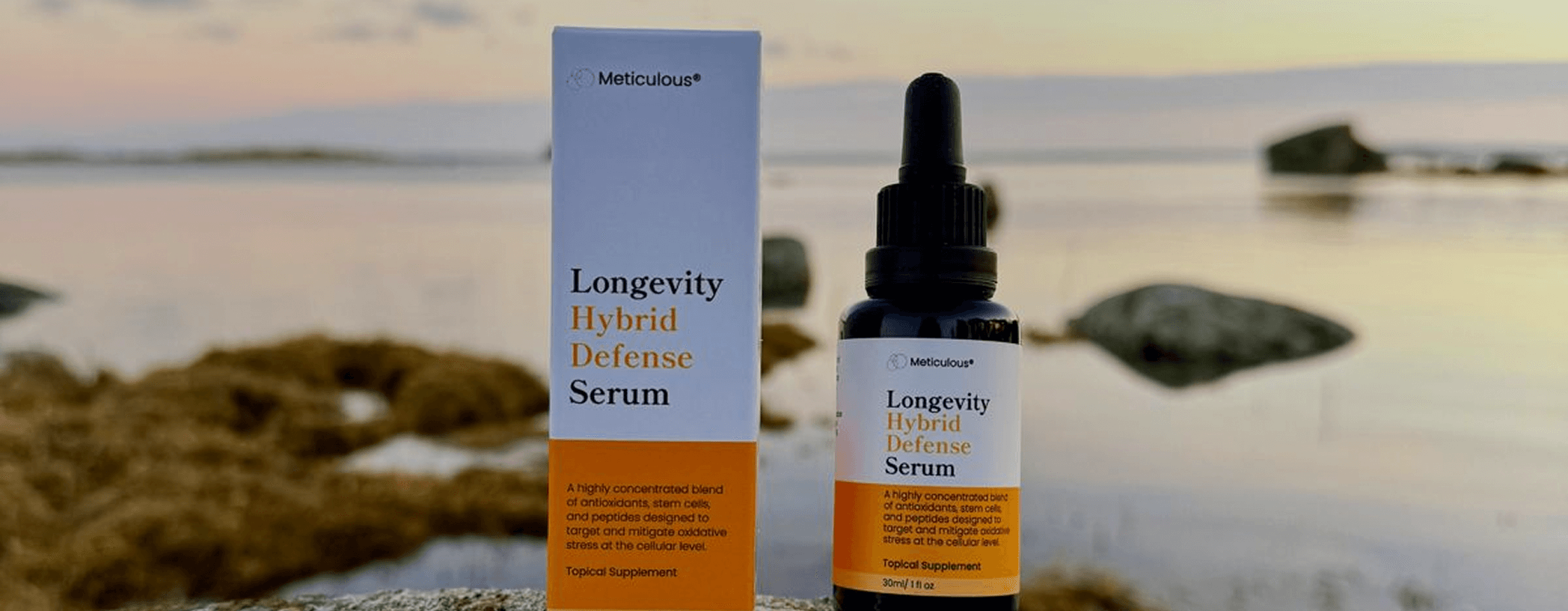 Serum bottle and box labeled 'Longevity Hybrid Defense Serum' on a rocky beach at sunset.