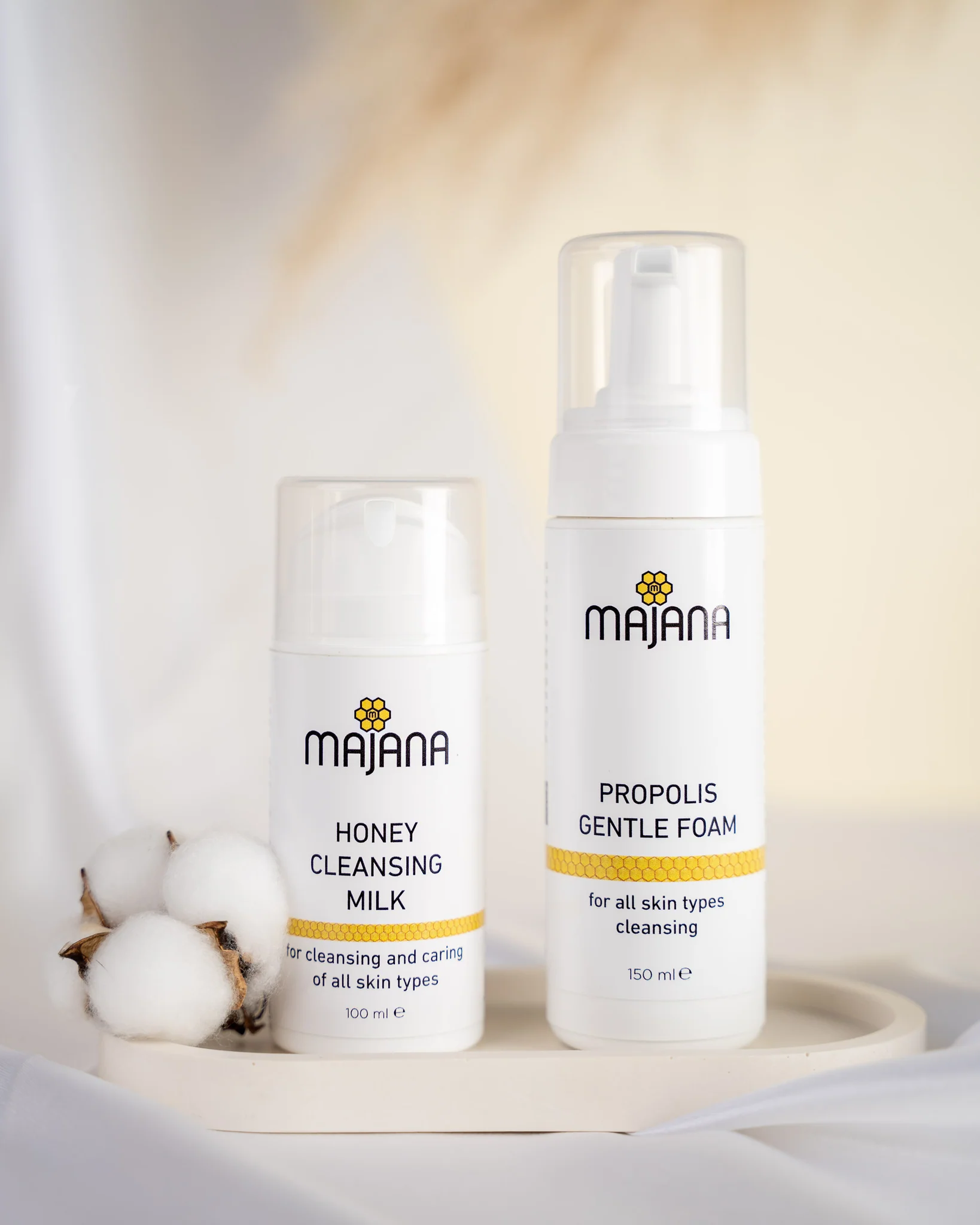 Two skincare bottles labeled 'Honey Cleansing Milk' and 'Propolis Gentle Foam' with cotton flowers.
