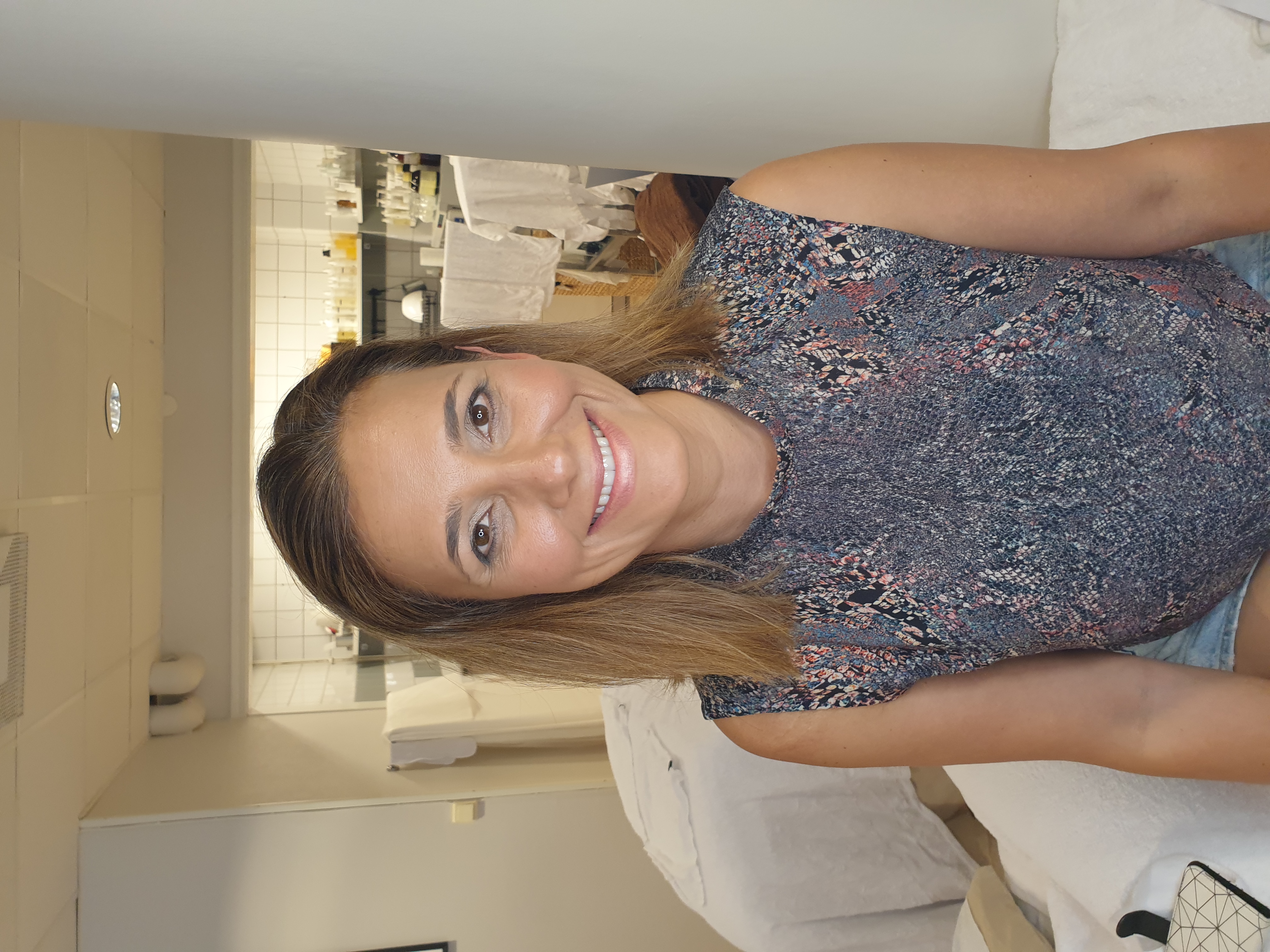 Smiling person sitting in a room with shelves and towels in the background.