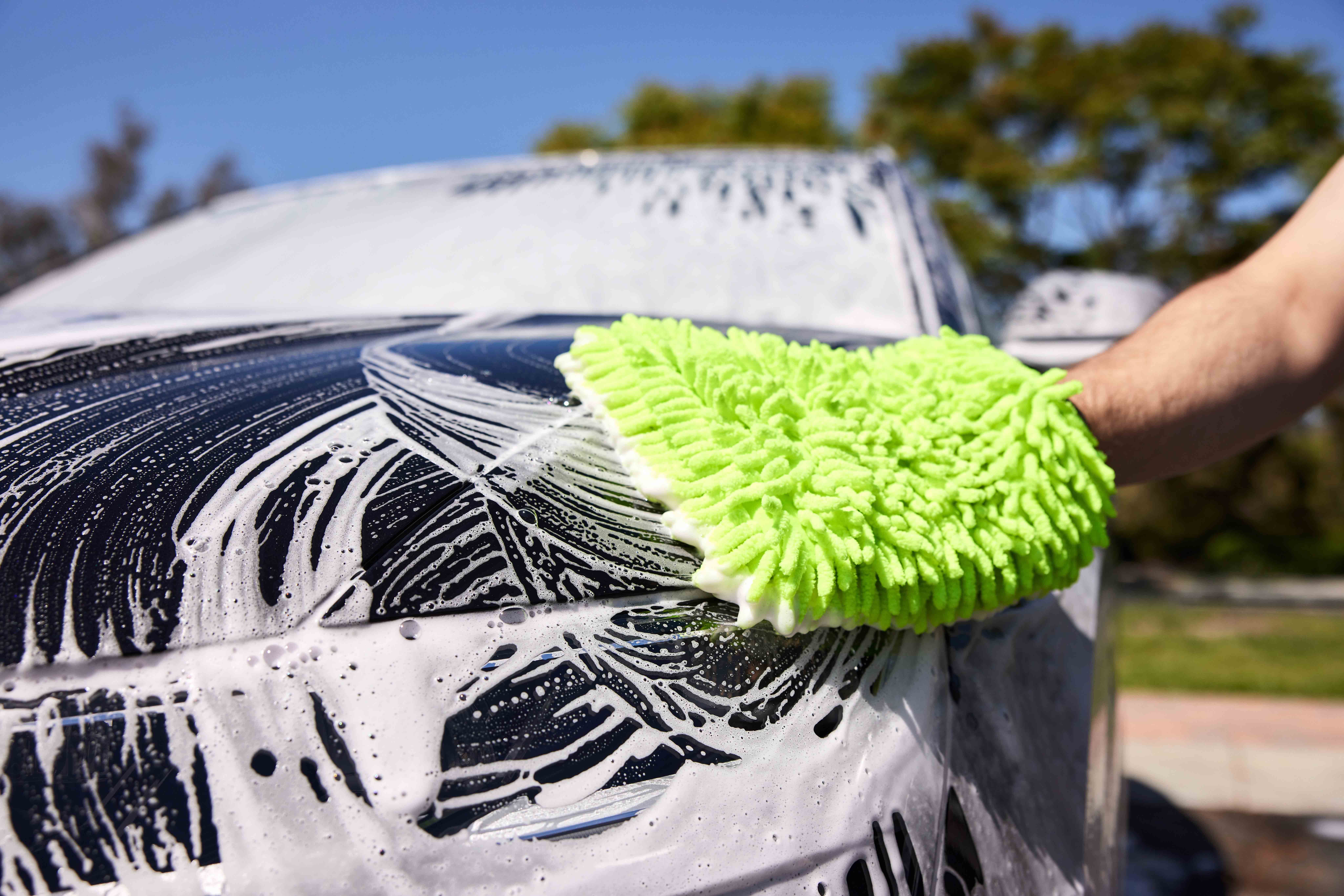 Person washing car with soapy water and green wash mitt.