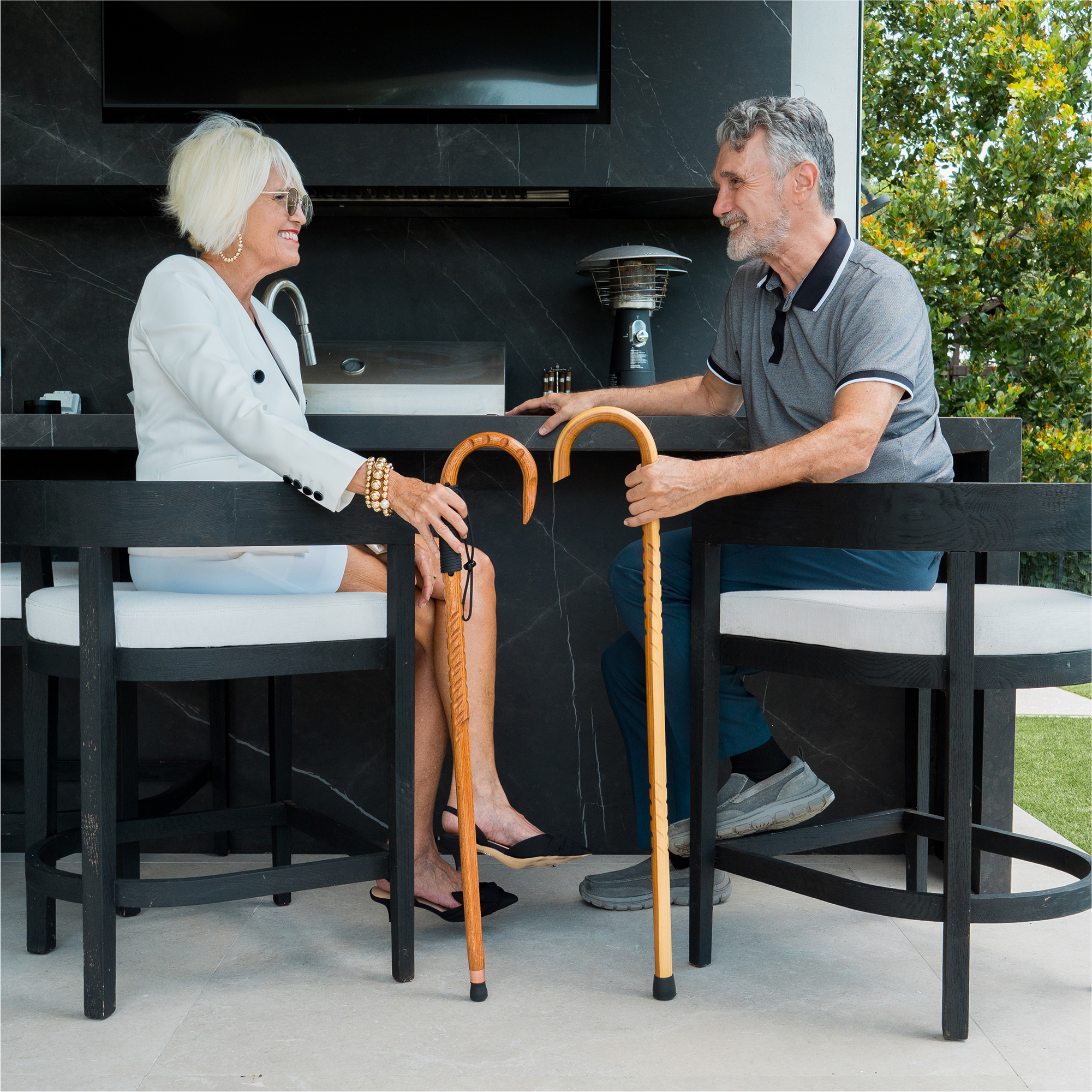 Two people sitting at a bar with walking canes, smiling at each other.