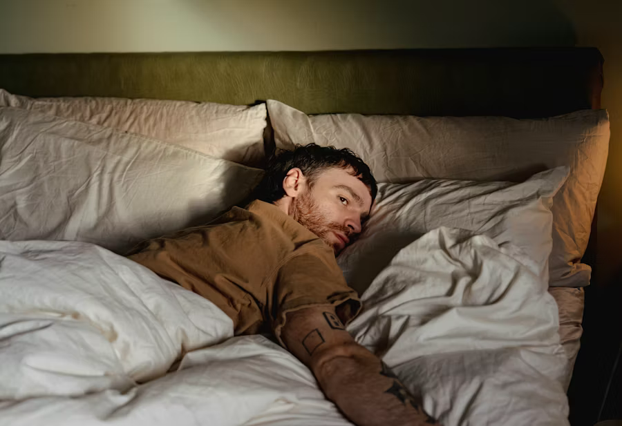 Person lying in bed looking over their shoulder at the camera.