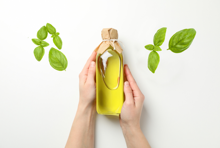 Hands holding a bottle of yellow liquid with basil leaves around.