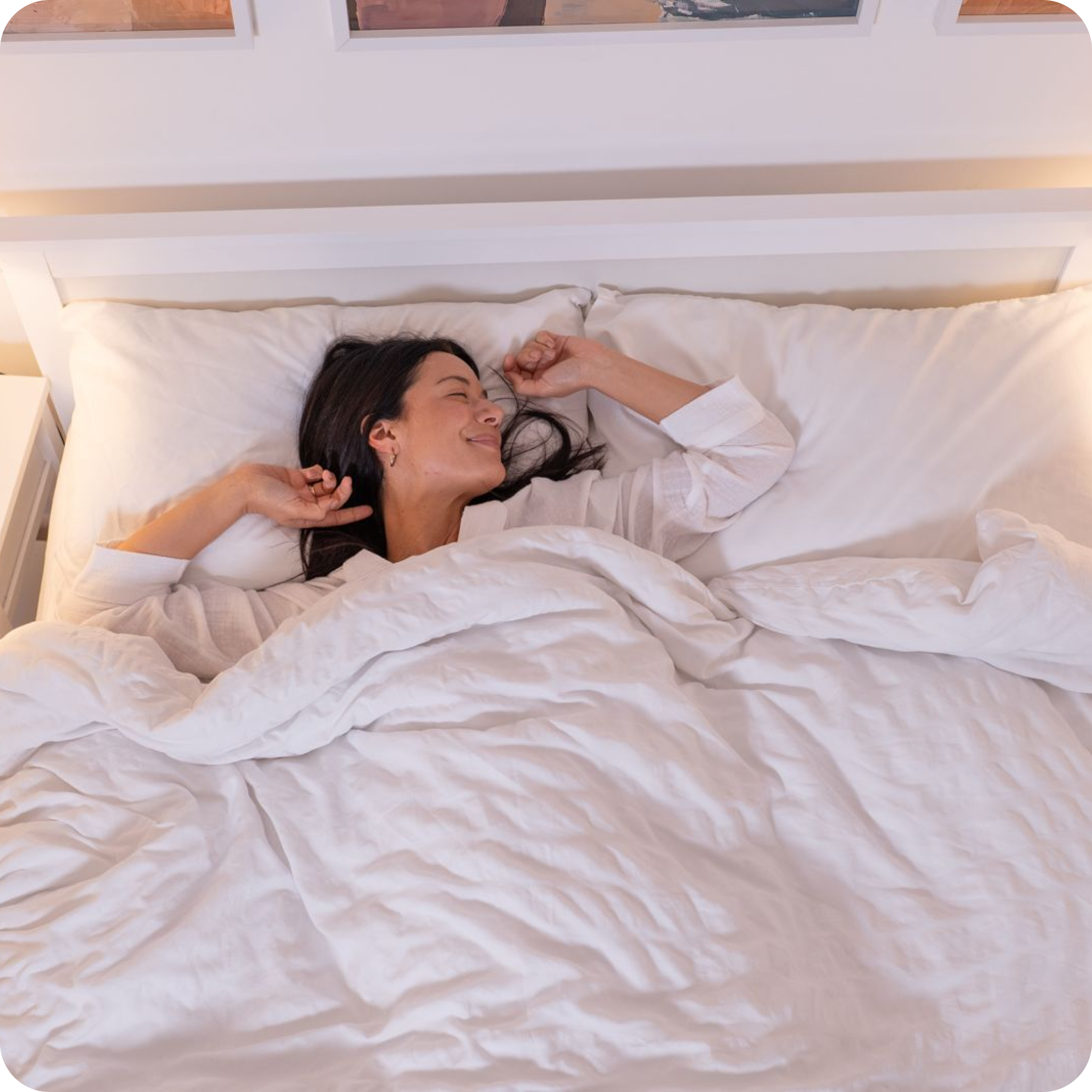 Person smiling while lying in bed under white blankets.