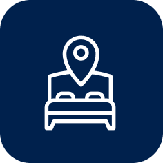 A white icon of a bed with a map pin above it on a dark blue background.