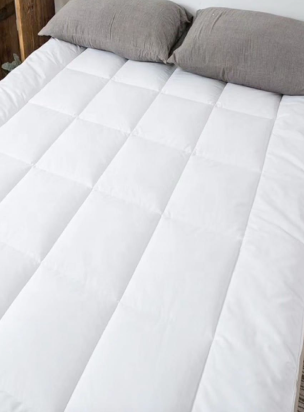White quilted bedspread with two gray pillows on a bed.