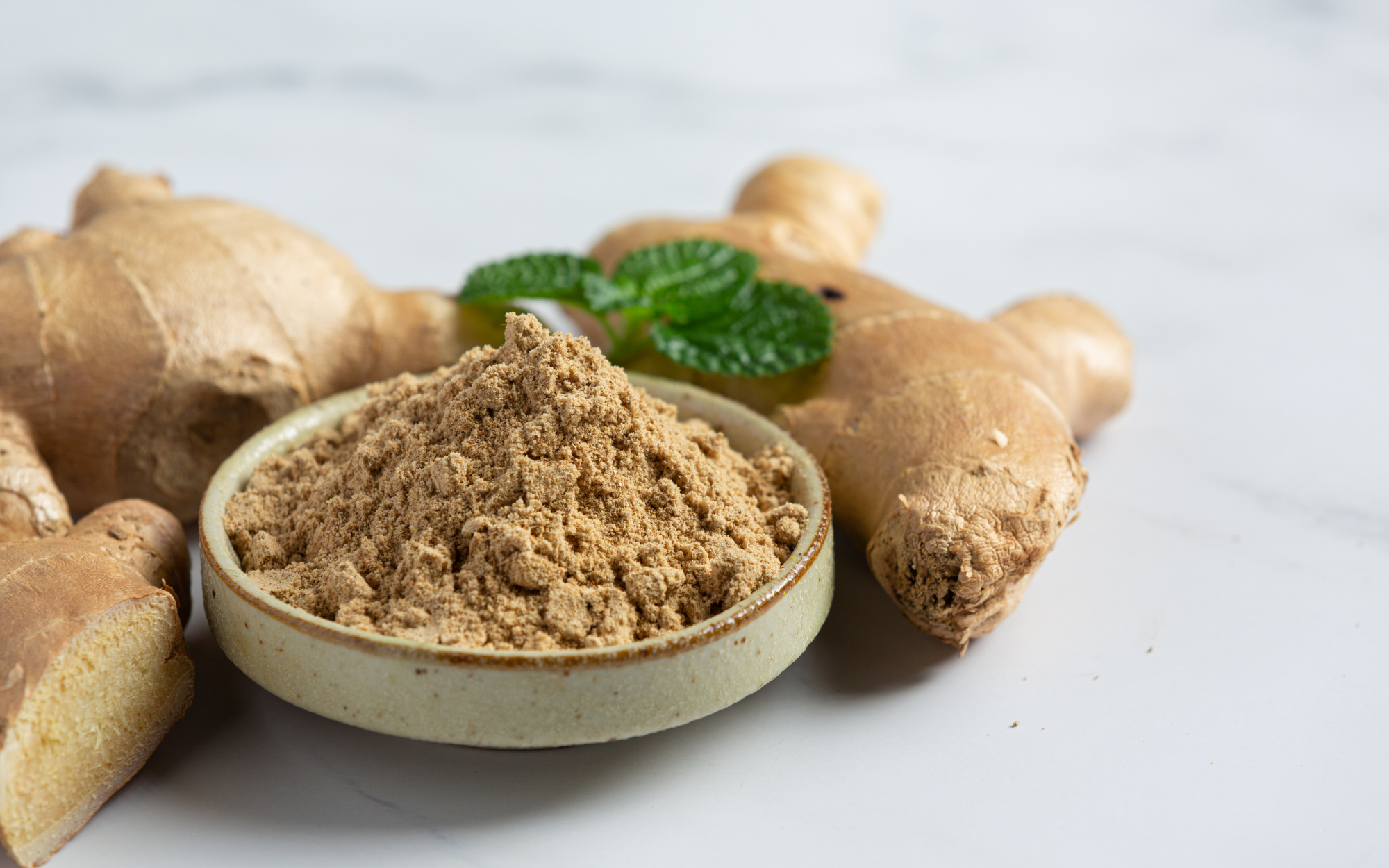 Bowl of ground ginger with fresh ginger roots and mint leaves.