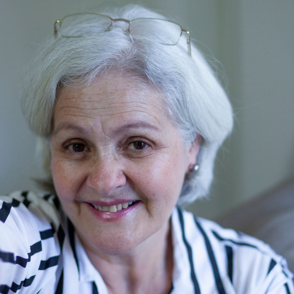 Older woman smiling, wearing glasses on her head and a striped shirt.