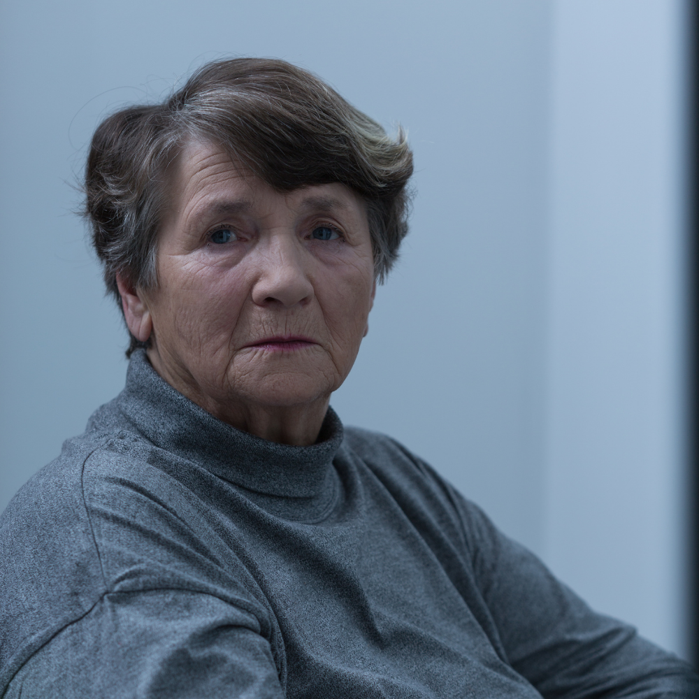 Elderly woman with short hair wearing a gray turtleneck, indoors.