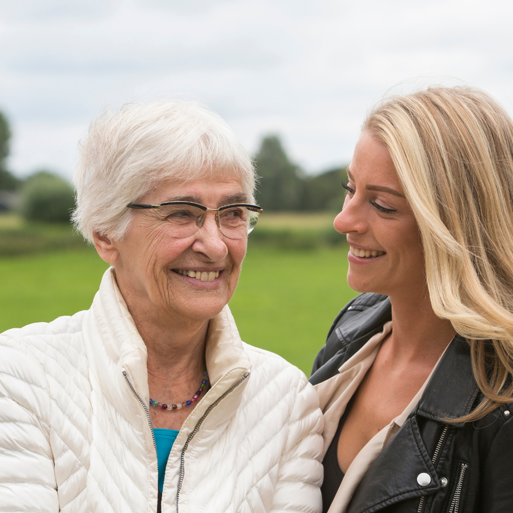 Two smiling women outdoors, one older and one younger, in casual jackets.
