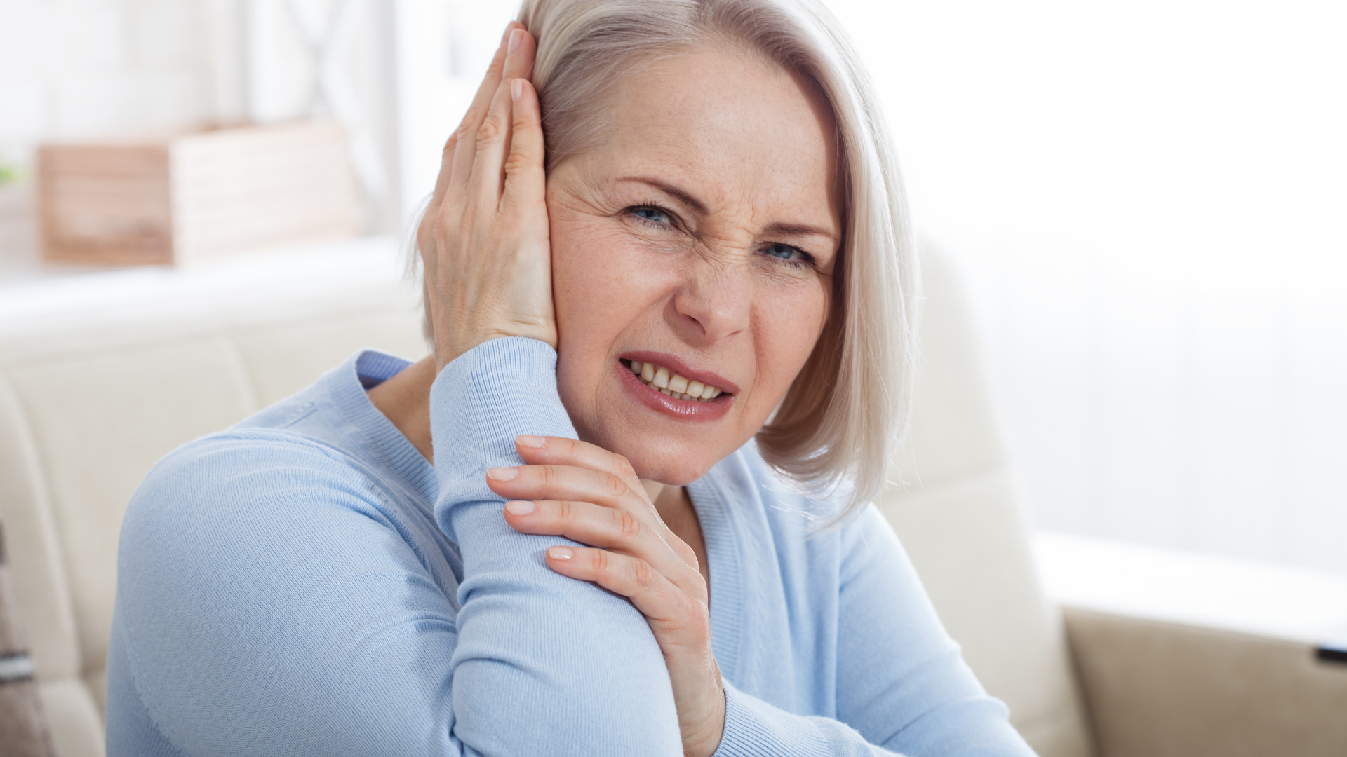 Person with short hair holding their ear and grimacing.