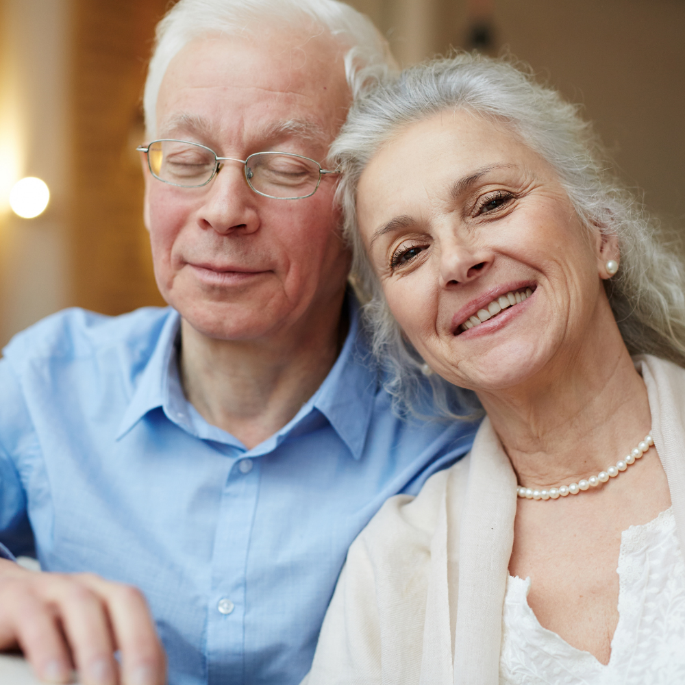 Smiling elderly couple sitting closely together indoors.