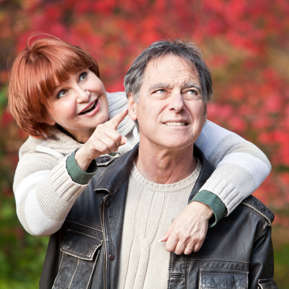 Smiling couple outdoors, woman pointing to the sky, autumn colors in background.