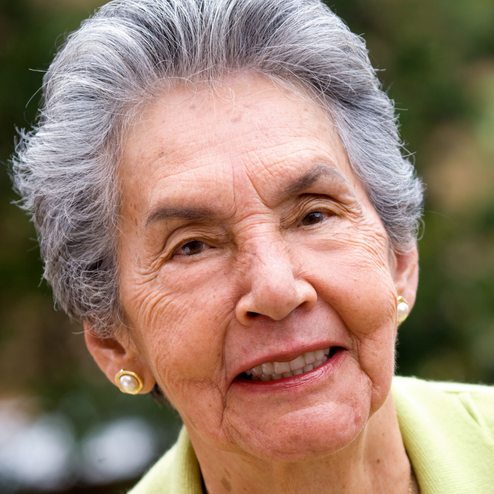 Elderly woman with short gray hair and earrings, smiling outdoors.